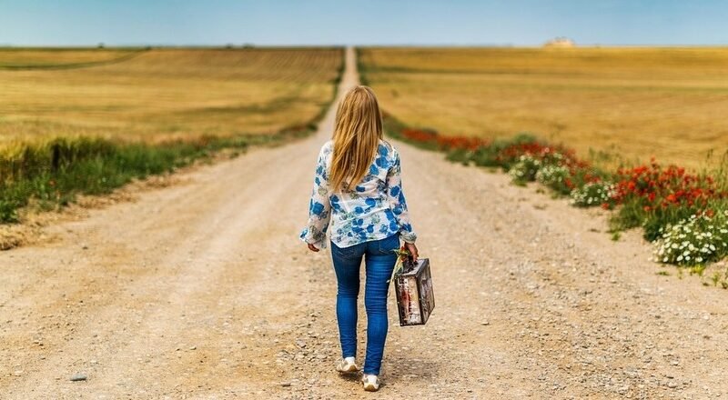 Nuevos caminos, mujer por un camino solitario cargando poco equipaje